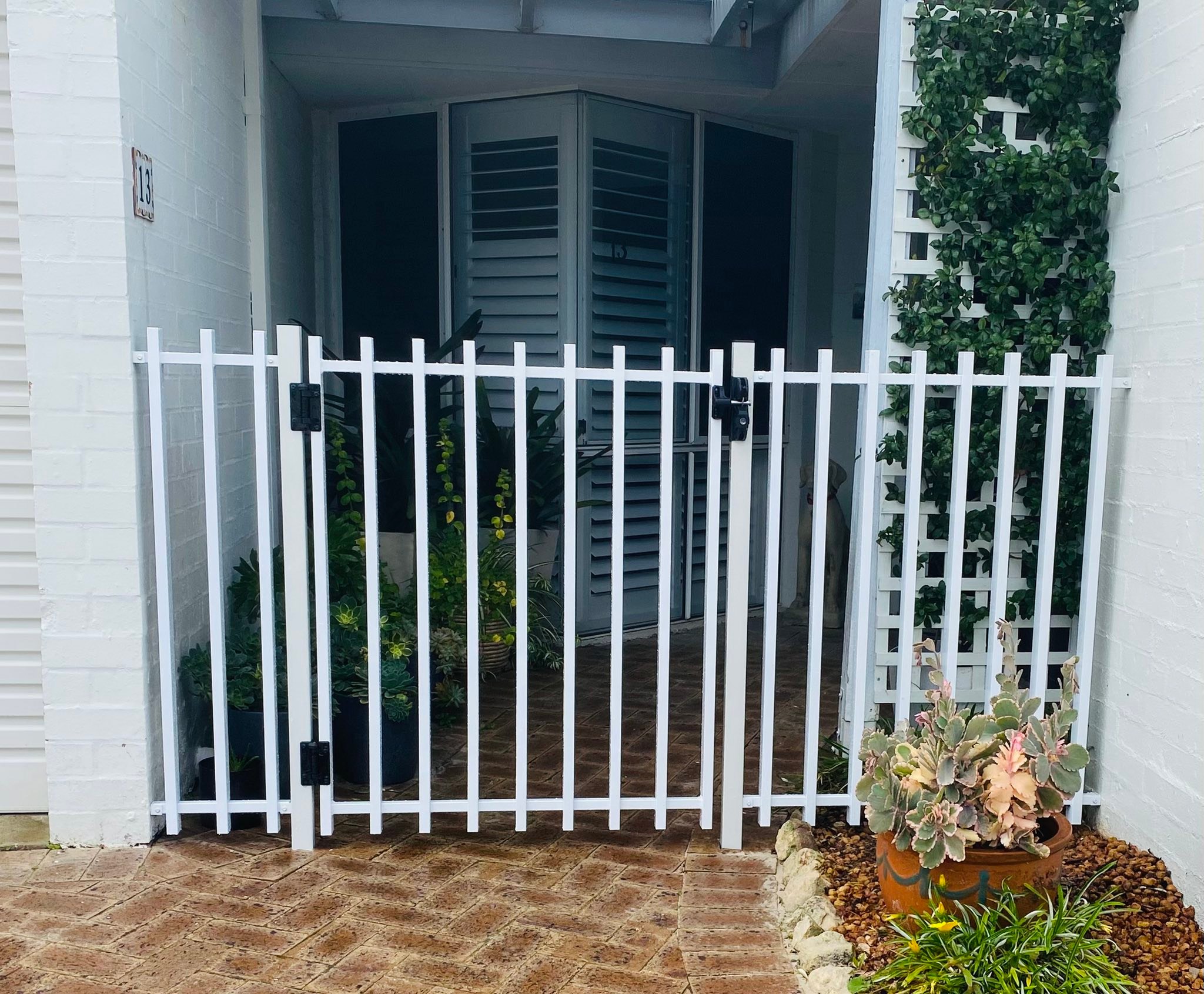White aluminium tubular pedestrian gate installed at a home entrance with garden and trellis