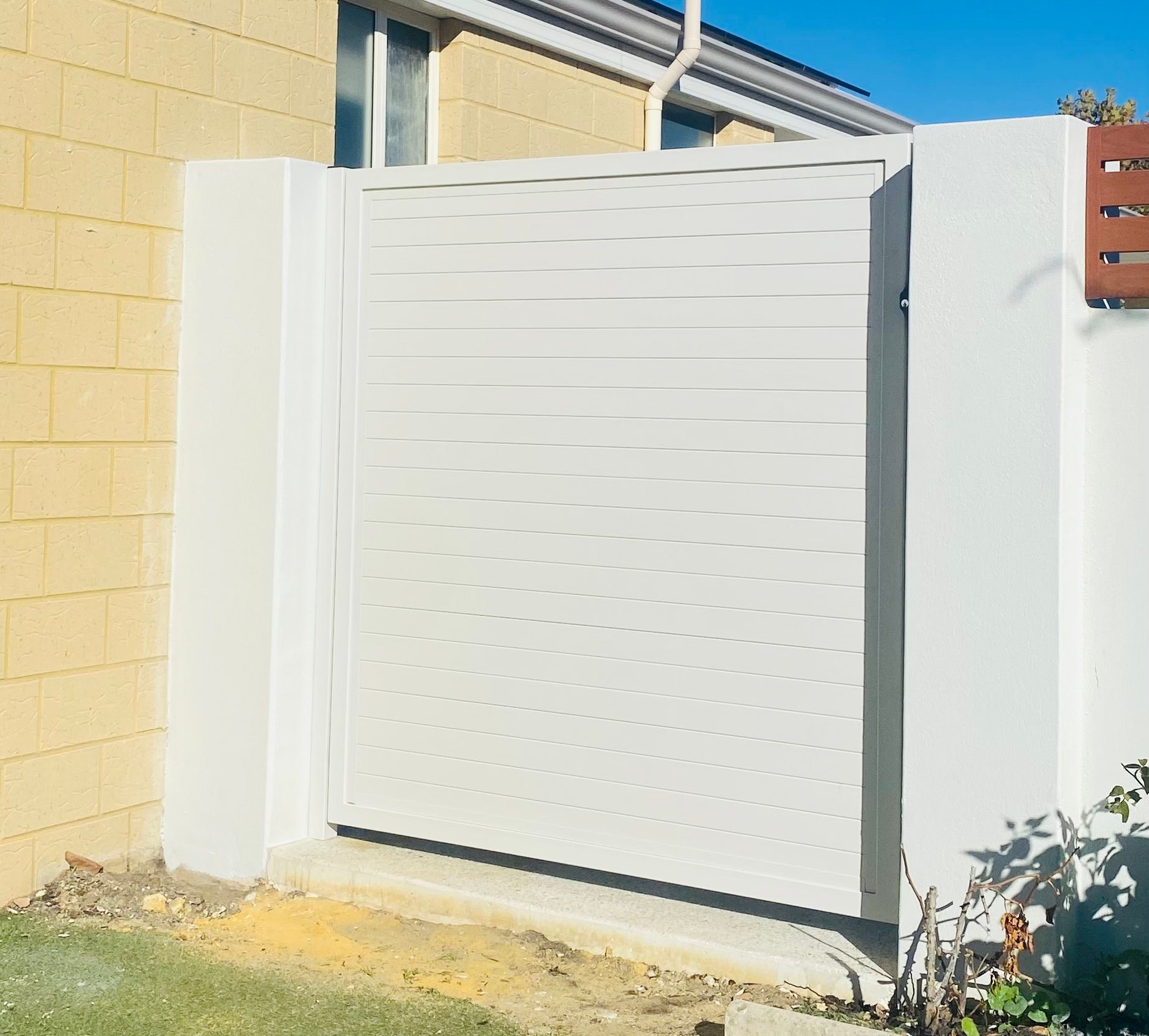 White horizontal-slat aluminium gate set into a rendered boundary wall